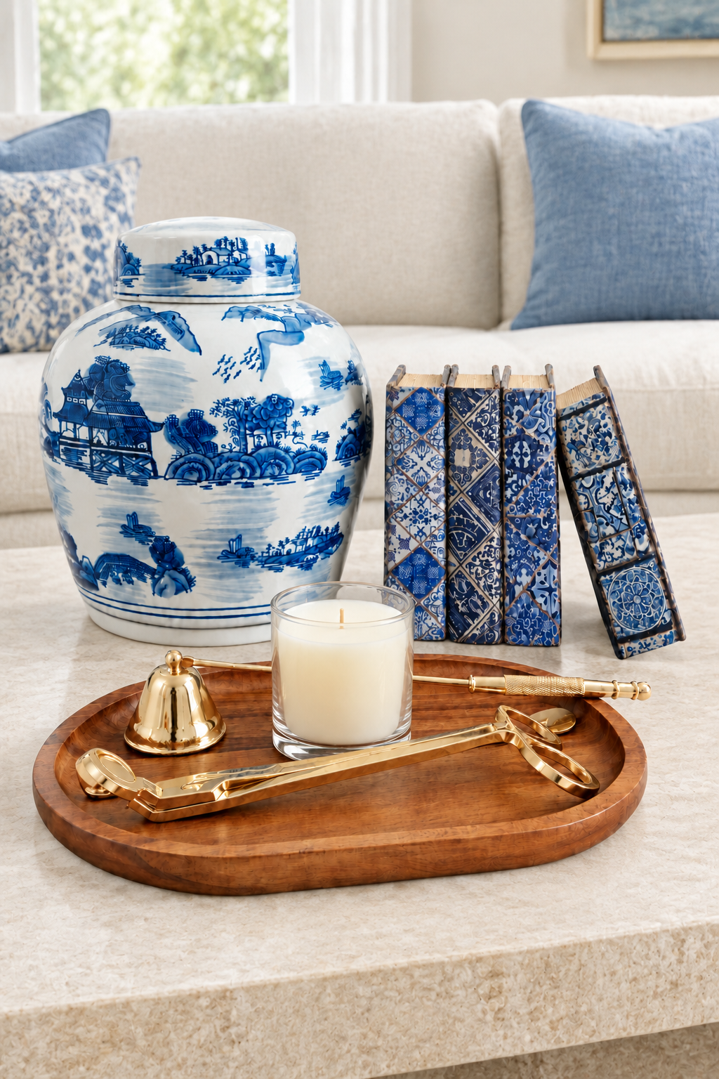 Blue and white ginger jar, patterned book boxes, candle, wood tray and gold-tone tools on a coffee table