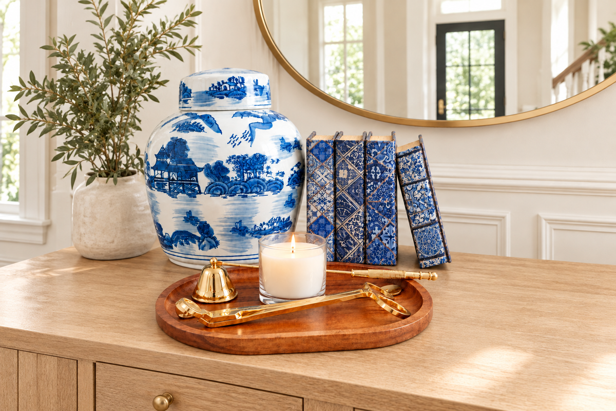 Blue and white ginger jar, book boxes and candle on a wood tray under a round mirror in an entryway