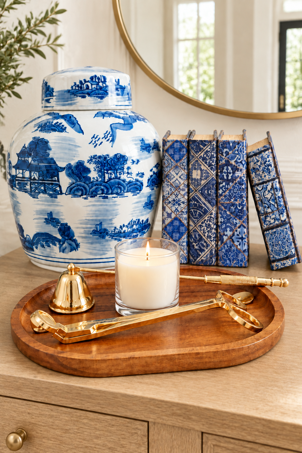 Close-up of a blue and white ginger jar and book boxes beside a lit candle on a wooden entryway console