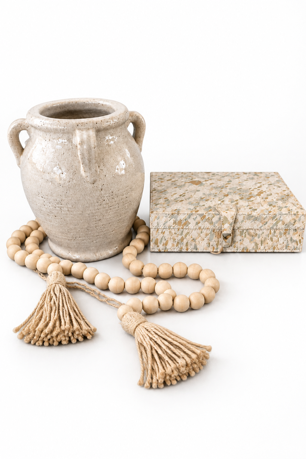 White crackle terracotta vase beside a closed cream and gold keepsake box and wood bead garland with tassels